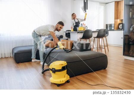 Modern yellow vacuum cleaner, busy. Two cleaning service workers are in domestic room Modern yellow vacuum cleaner, busy. Two cleaning service workers are in domestic room 135832430