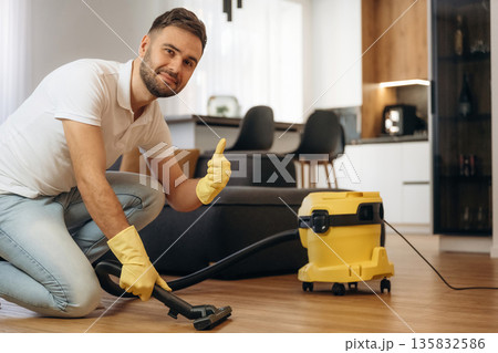 Using vacuum cleaner. Male professional cleaning service worker is domestic room Using vacuum cleaner. Male professional cleaning service worker is domestic room 135832586