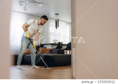 Standing and moping the floor. Male professional cleaning service worker is domestic room Standing and moping the floor. Male professional cleaning service worker is domestic room 135832612