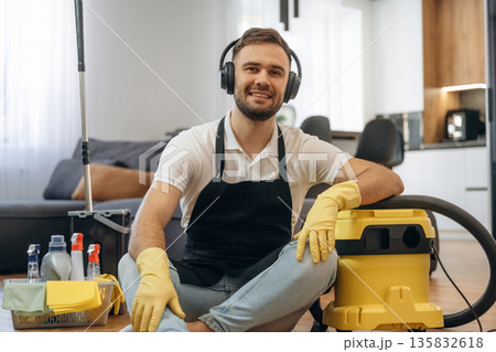 Enjoying music. Sitting. Male professional cleaning service worker is domestic room Enjoying music. Sitting. Male professional cleaning service worker is domestic room 135832618