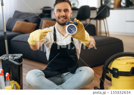 Blue clock in hand. Male professional cleaning service worker is domestic room Blue clock in hand. Male professional cleaning service worker is domestic room 135832634