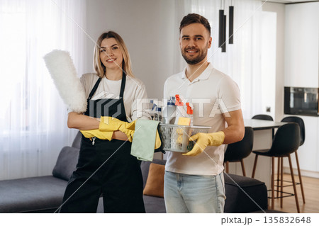 Woman is in uniform, standing. Two cleaning service workers are in domestic room Woman is in uniform, standing. Two cleaning service workers are in domestic room 135832648
