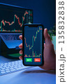 Trader hand holding smartphone with stock market or crypto trading app on screen 135832838
