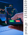 A trader holds a smartphone with a stock market trading app on the screen 135832839