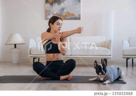 Stretching warm ups. Woman with pug dog is doing yoga at home Stretching warm ups. Woman with pug dog is doing yoga at home 135832888