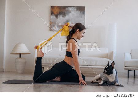 Yellow tape, stretching. Woman with pug dog is doing yoga at home Yellow tape, stretching. Woman with pug dog is doing yoga at home 135832897