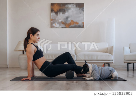 Side view. Woman with pug dog is doing yoga at home 135832903