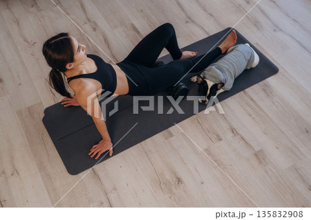 Taking a break. Woman with pug dog is doing yoga at home Taking a break. Woman with pug dog is doing yoga at home 135832908