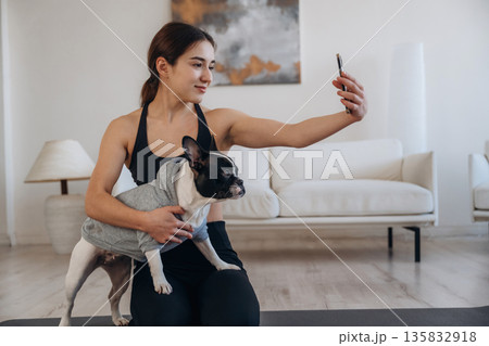 Making selfie. Sportive woman in yoga clothes is with pug dog at home Making selfie. Sportive woman in yoga clothes is with pug dog at home 135832918