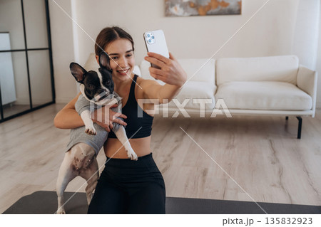 Doing selfie. Sportive woman in yoga clothes is with pug dog at home 135832923
