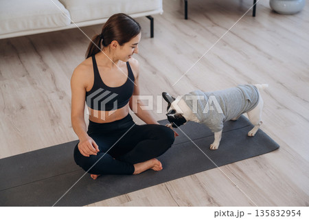 Lotus pose, meditation. Woman with pug dog is doing yoga at home 135832954