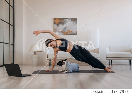 Looking at laptop, online learning. Woman with pug dog is doing yoga at home Looking at laptop, online learning. Woman with pug dog is doing yoga at home 135832958