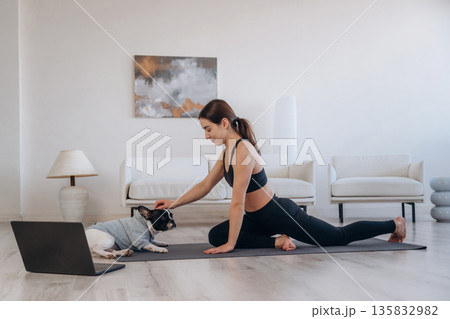 Laptop is on the floor. Woman with pug dog is doing yoga at home 135832982