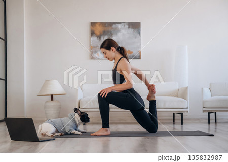 Laptop is on the floor. Woman with pug dog is doing yoga at home Laptop is on the floor. Woman with pug dog is doing yoga at home 135832987