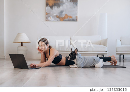 Searching the web on laptop. Woman with pug dog is doing yoga at home 135833016