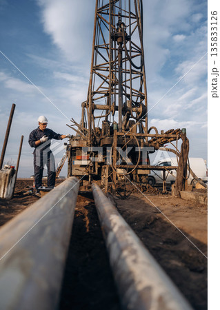Walkie talkie in hand. Construction worker is near boring drilling machine Walkie talkie in hand. Construction worker is near boring drilling machine 135833126