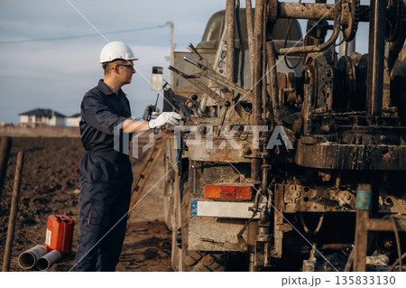 Operator is standing and making adjustments. Construction worker is near boring drilling machine Operator is standing and making adjustments. Construction worker is near boring drilling machine 135833130