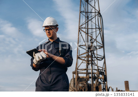 Black color digital tablet is in hands. Construction worker is near boring drilling machine Black color digital tablet is in hands. Construction worker is near boring drilling machine 135833141