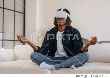 Lotus pose, meditation. Black man in virtual reality glasses at home 135833427