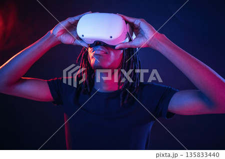 Blue and red colors. African American guy is with virtual reality glasses in neon room Blue and red colors. African American guy is with virtual reality glasses in neon room 135833440