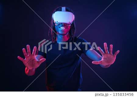 Playing the game. African American guy is with virtual reality glasses in neon room 135833456