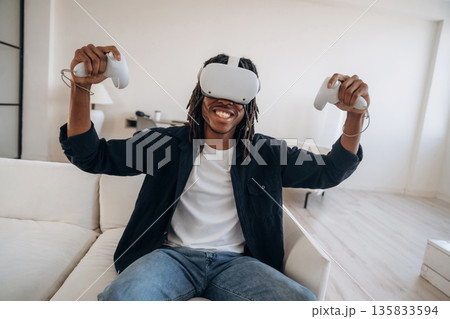 Won the game, celebrating. Black man in virtual reality glasses at home Won the game, celebrating. Black man in virtual reality glasses at home 135833594