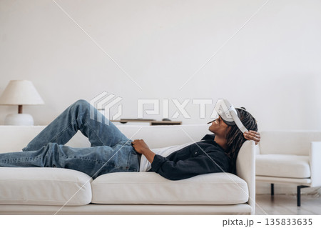 Resting, lying down and watching. Black man in virtual reality glasses at home Resting, lying down and watching. Black man in virtual reality glasses at home 135833635