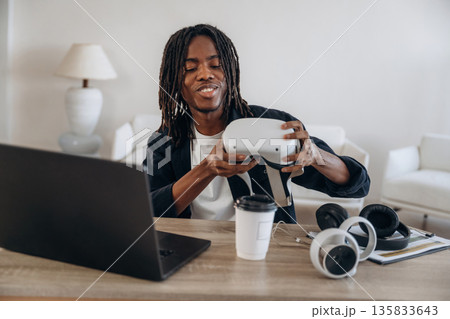 Wearing headset. Young man is sitting by table with laptop and virtual reality glasses 135833643