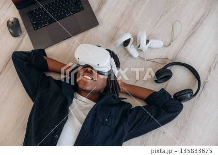 Computer nearby. Top view of man that is lying down on floor in virtual reality headset 135833675