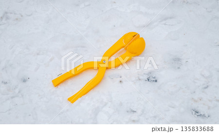 Yellow plastic snowball maker tool resting on a blanket of white snow outdoors. Winter weather toy for children and adults to enjoy cold season fun. Yellow plastic snowball maker tool resting on a blanket of white snow outdoors. Winter weather toy for children and adults to enjoy cold season fun. 135833688