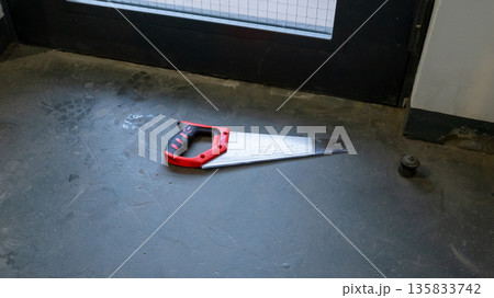 Hand saw lying on concrete floor in apartment building entrance. Tool for construction work or repair. Concept of home improvement and DIY. Hand saw lying on concrete floor in apartment building entrance. Tool for construction work or repair. Concept of home improvement and DIY. 135833742