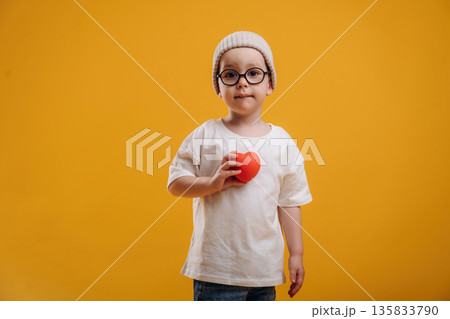 Small heart shaped toy. Cute little boy is against yellow background 135833790