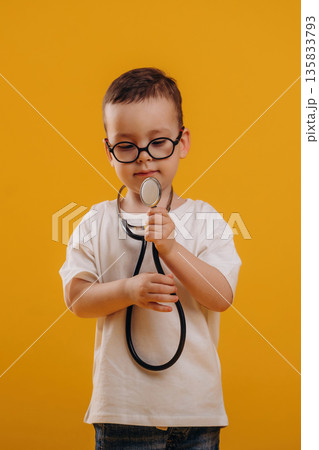 Playing doctor, with stethoscope. Cute little boy is against yellow background Playing doctor, with stethoscope. Cute little boy is against yellow background 135833793