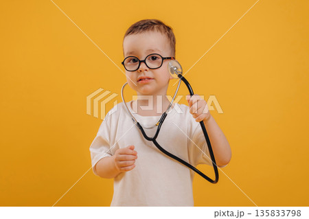 Stethoscope in hands. Cute little boy is against yellow background Stethoscope in hands. Cute little boy is against yellow background 135833798