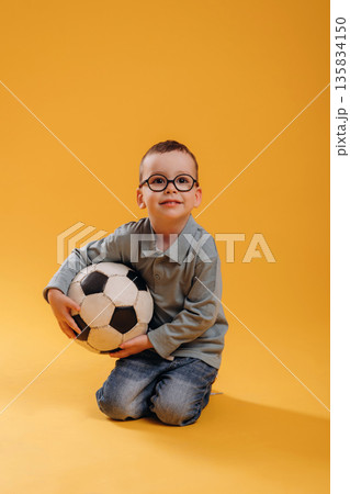 Soccer ball in hands. Cute little boy is against yellow background Soccer ball in hands. Cute little boy is against yellow background 135834150