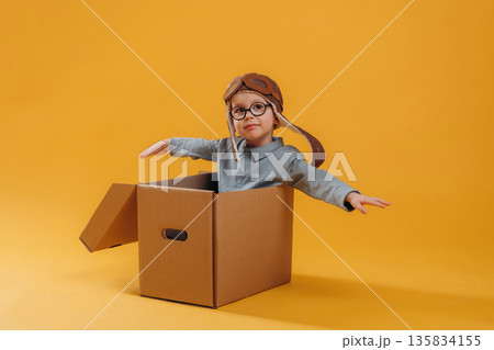 Aviator hat, in the box. Cute little boy is against yellow background 135834155