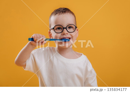 Cleaning teeth by toothbrush. Cute little boy is against yellow background Cleaning teeth by toothbrush. Cute little boy is against yellow background 135834177