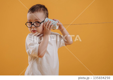 Tin can telephone is in hands. Cute little boy is against yellow background Tin can telephone is in hands. Cute little boy is against yellow background 135834250