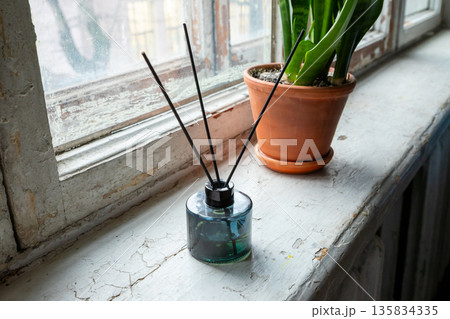 Scent diffuser with reed sticks on old windowsill near houseplant for home fragrance and aromatherapy. Relax and cozy home. old housing stock 135834335