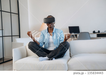On the sofa in virtual reality headset. Woman is at home in domestic room On the sofa in virtual reality headset. Woman is at home in domestic room 135834443