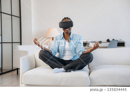On the sofa in virtual reality headset. Woman is at home in domestic room On the sofa in virtual reality headset. Woman is at home in domestic room 135834445