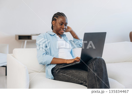Working by using laptop, sitting on sofa. Woman is at home in domestic room Working by using laptop, sitting on sofa. Woman is at home in domestic room 135834467