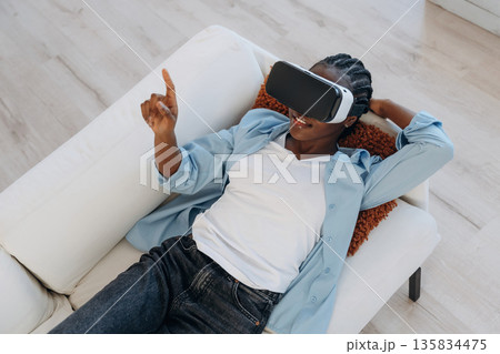 Relaxing, lying down on sofa in VR headset. Woman is at home in domestic room Relaxing, lying down on sofa in VR headset. Woman is at home in domestic room 135834475