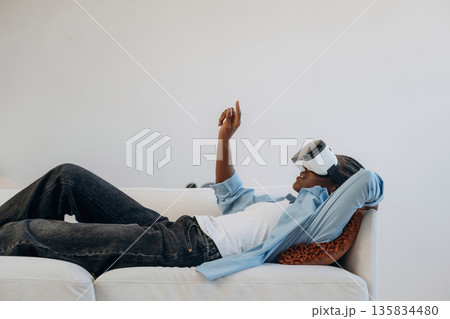 Side view, lying down and wearing VR headset. Woman is at home in domestic room Side view, lying down and wearing VR headset. Woman is at home in domestic room 135834480