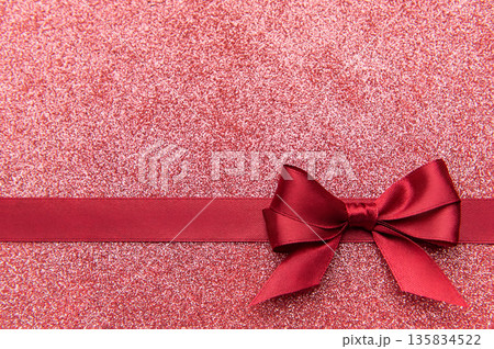 Red satin bow on glistening pink glitter background Red satin bow on glistening pink glitter background 135834522