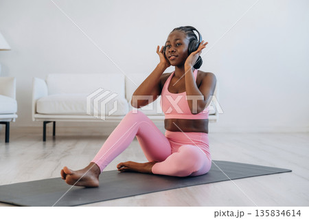 Listening to the music in headphones. Woman is doing yoga at home Listening to the music in headphones. Woman is doing yoga at home 135834614