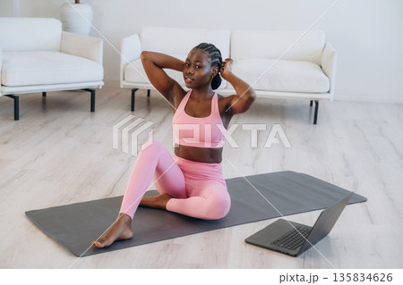 On the yoga mat, sitting, laptop on floor. Woman is doing yoga at home 135834626