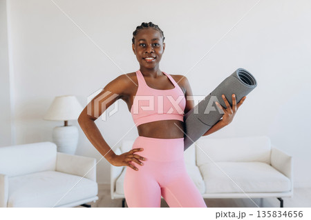 Mat is in hand, standing. Woman is doing yoga at home 135834656