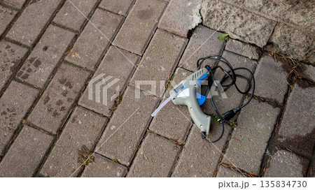 Glue gun on a paved stone surface. Craft tool for repair, construction or creative project, decorations. Crafting equipment for hobbyist. Glue gun on a paved stone surface. Craft tool for repair, construction or creative project, decorations. Crafting equipment for hobbyist. 135834730