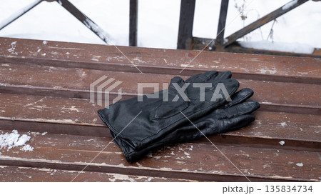 pair of black leather gloves on weathered wooden bench with snow. Winter accessory for cold weather protection and style. 135834734